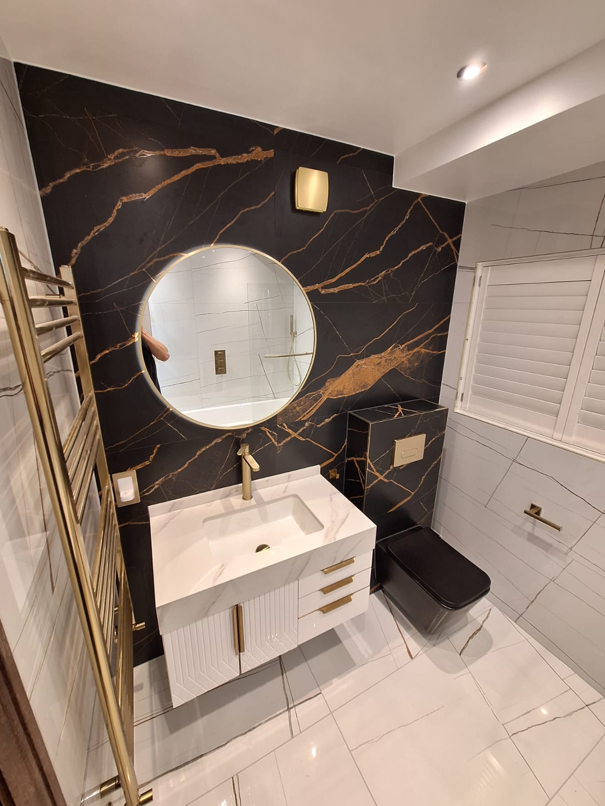 Finished en-suite bathroom with black Portoro feature wall, brushed brass radiator and white vanity