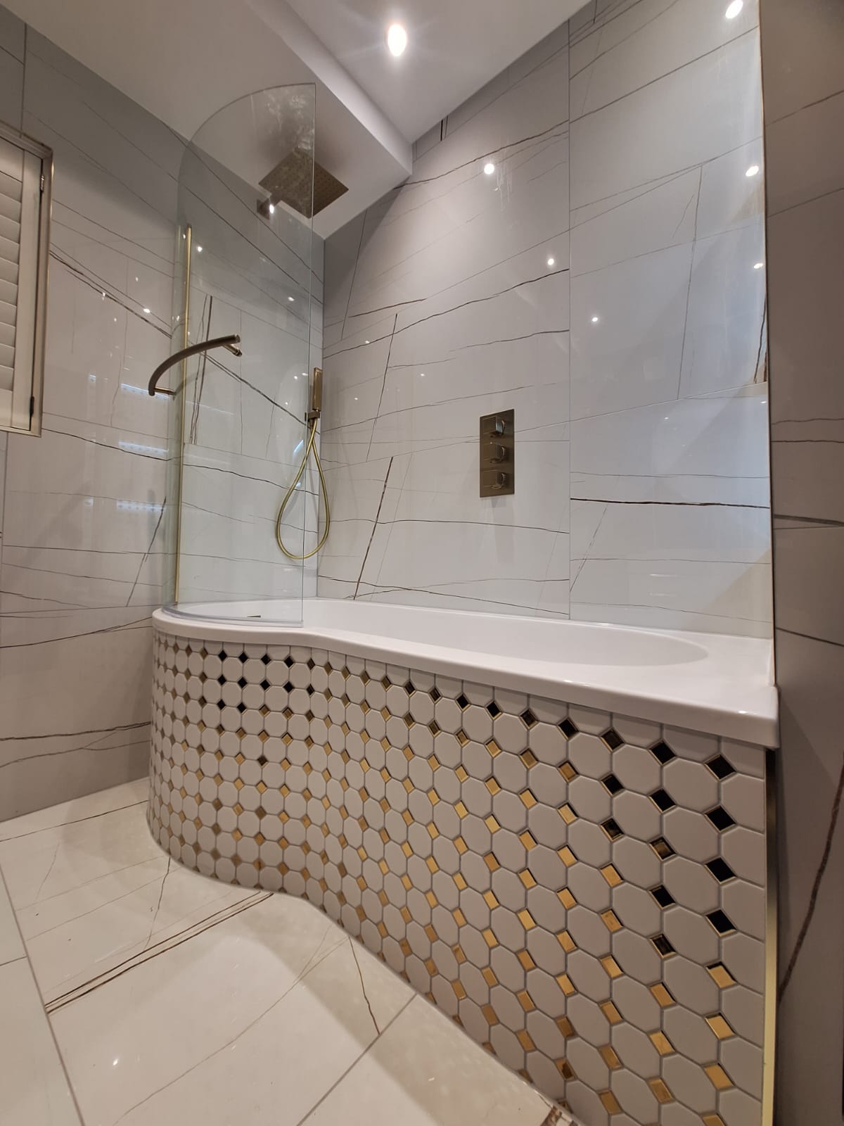 Curved bath with hex mosaic skirt in gold and white, brushed brass shower screen