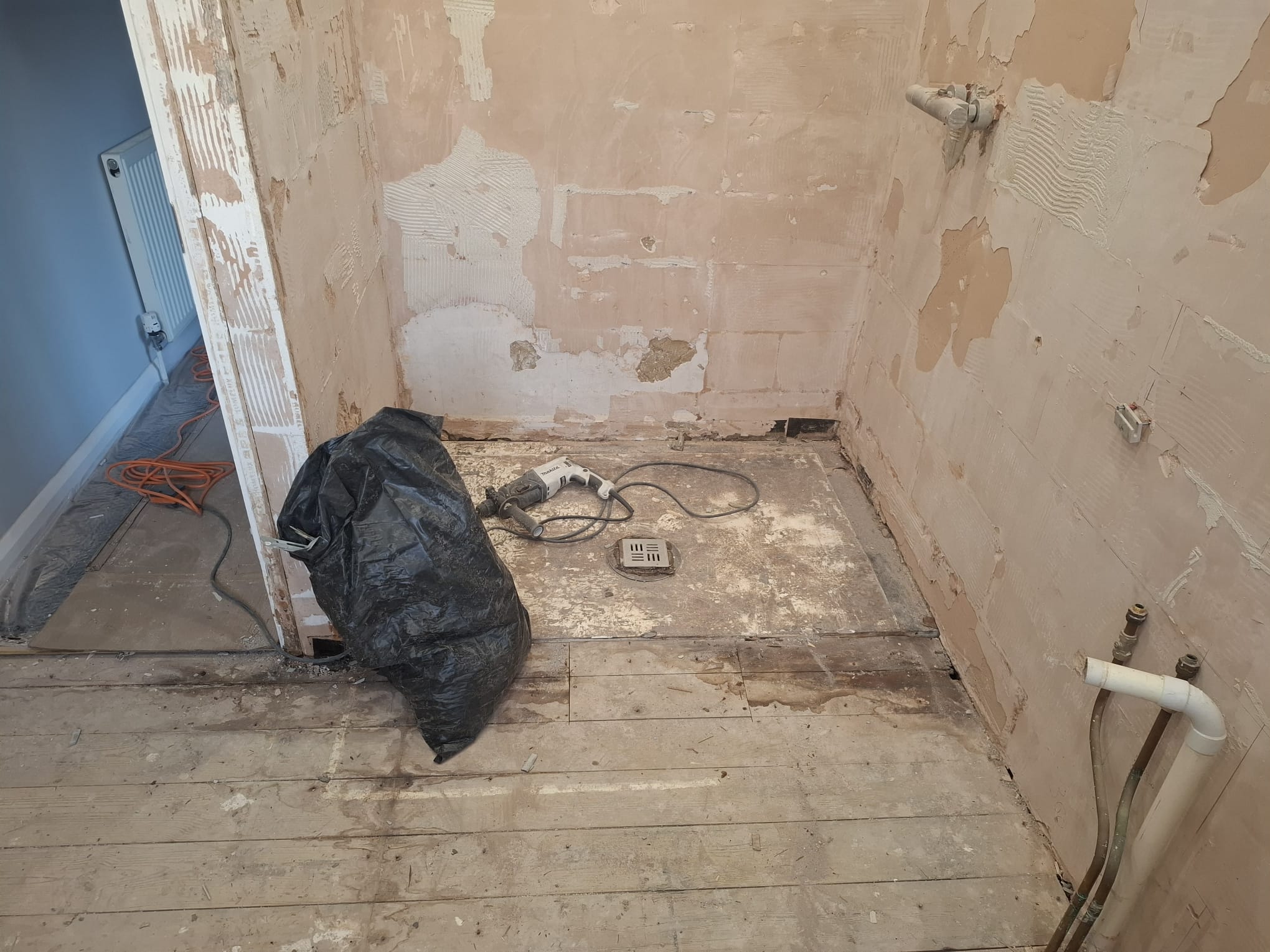 During renovation, stripped shower zone with tools and rubbish bag